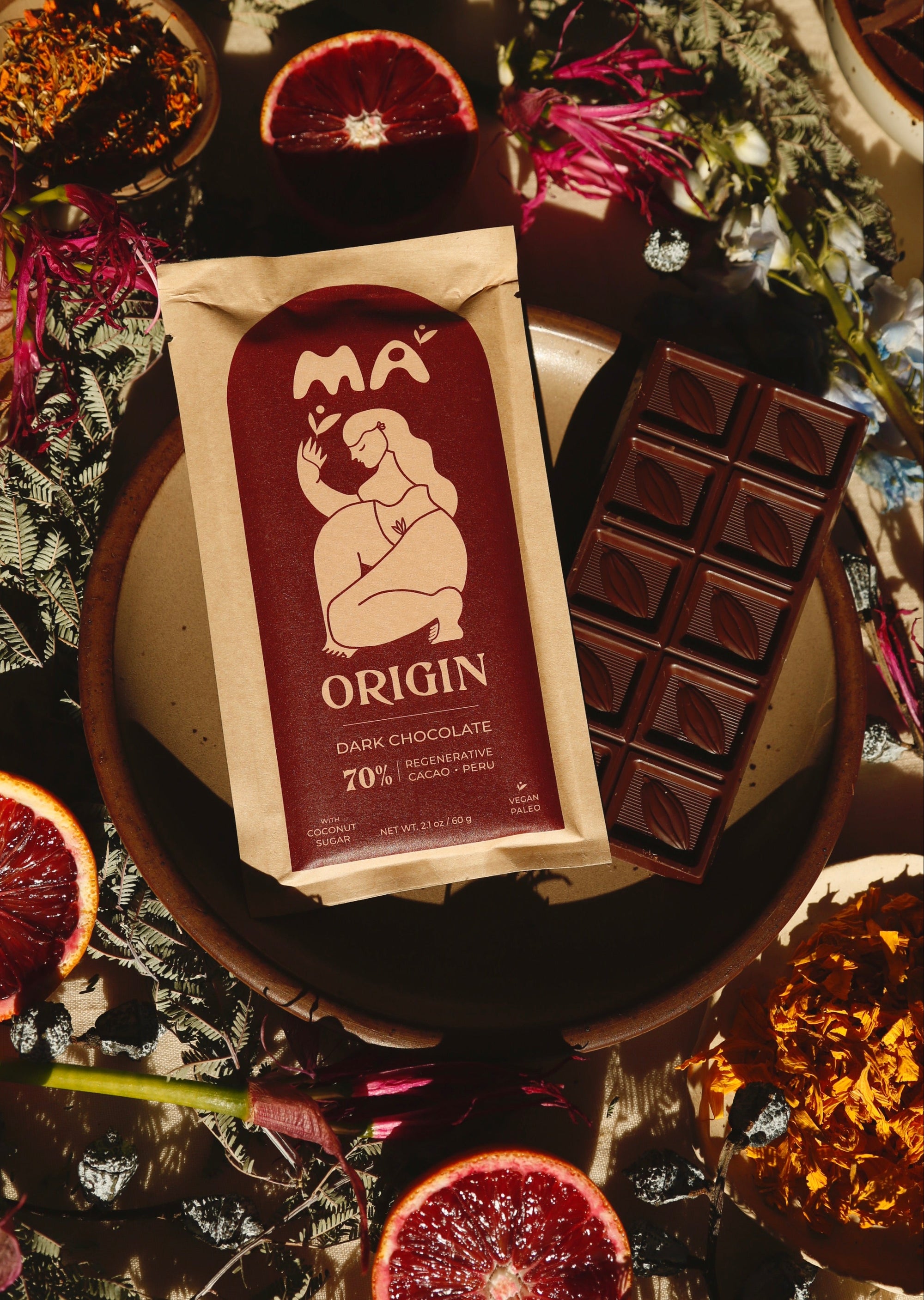 MA Origin dark chocolate bar on a decorative surface with fruits and flowers