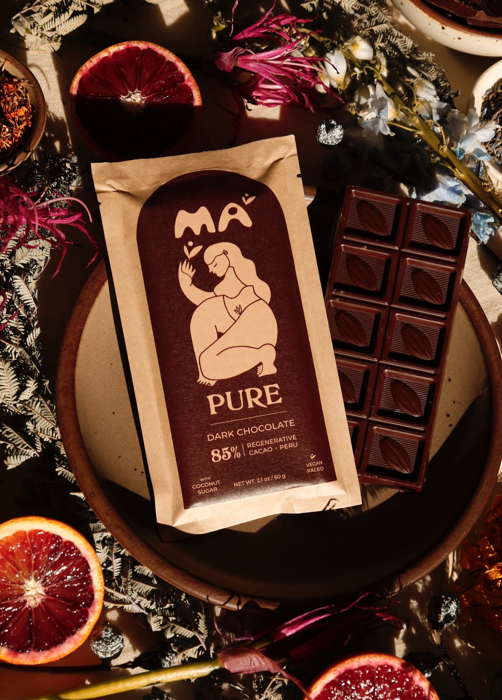 Pure dark chocolate bars with packaging on a decorative surface with flowers and fruits.