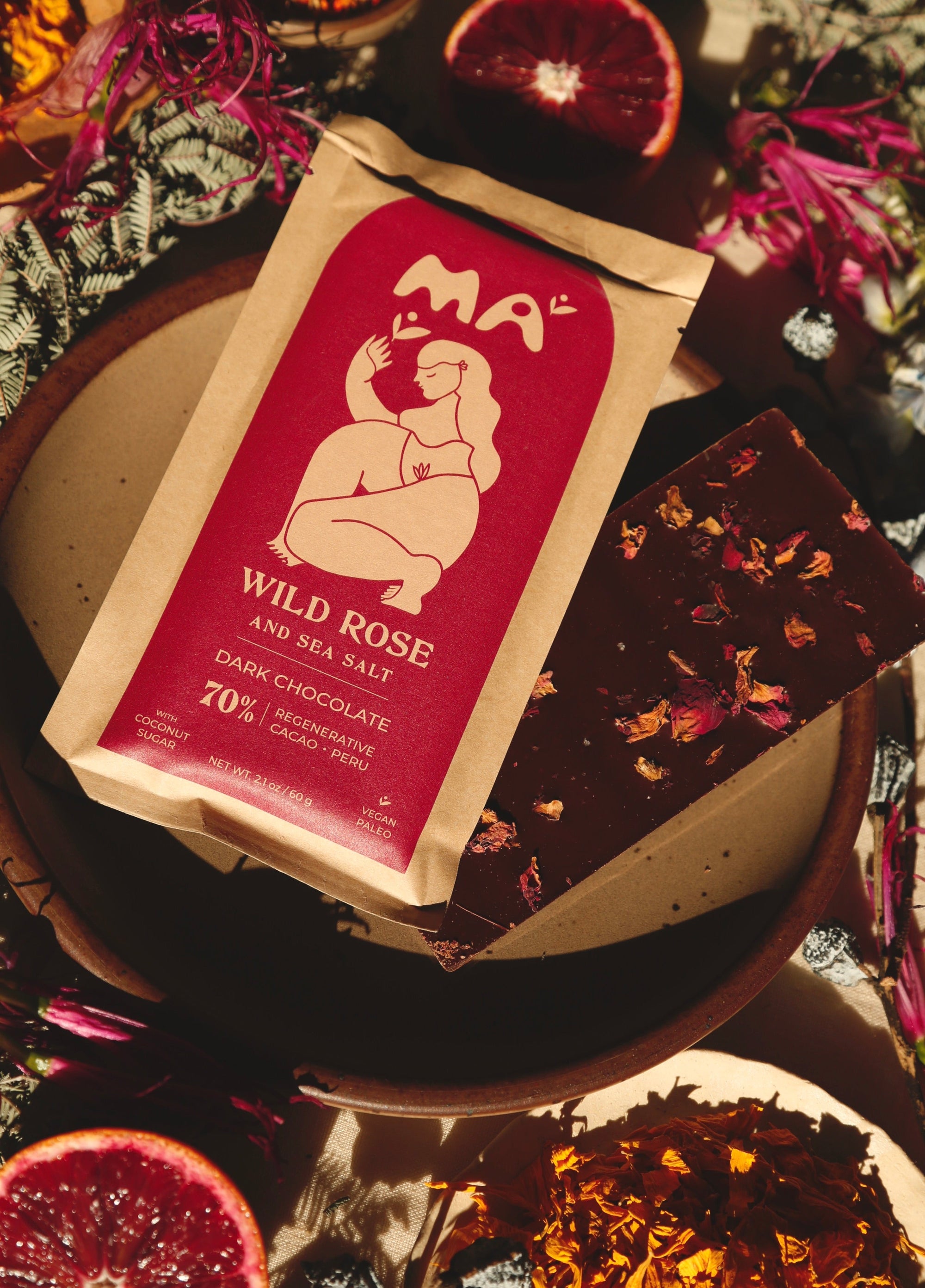 Bar of Wild Rose and Sea Salt dark chocolate on a decorative plate with flowers and fruits.